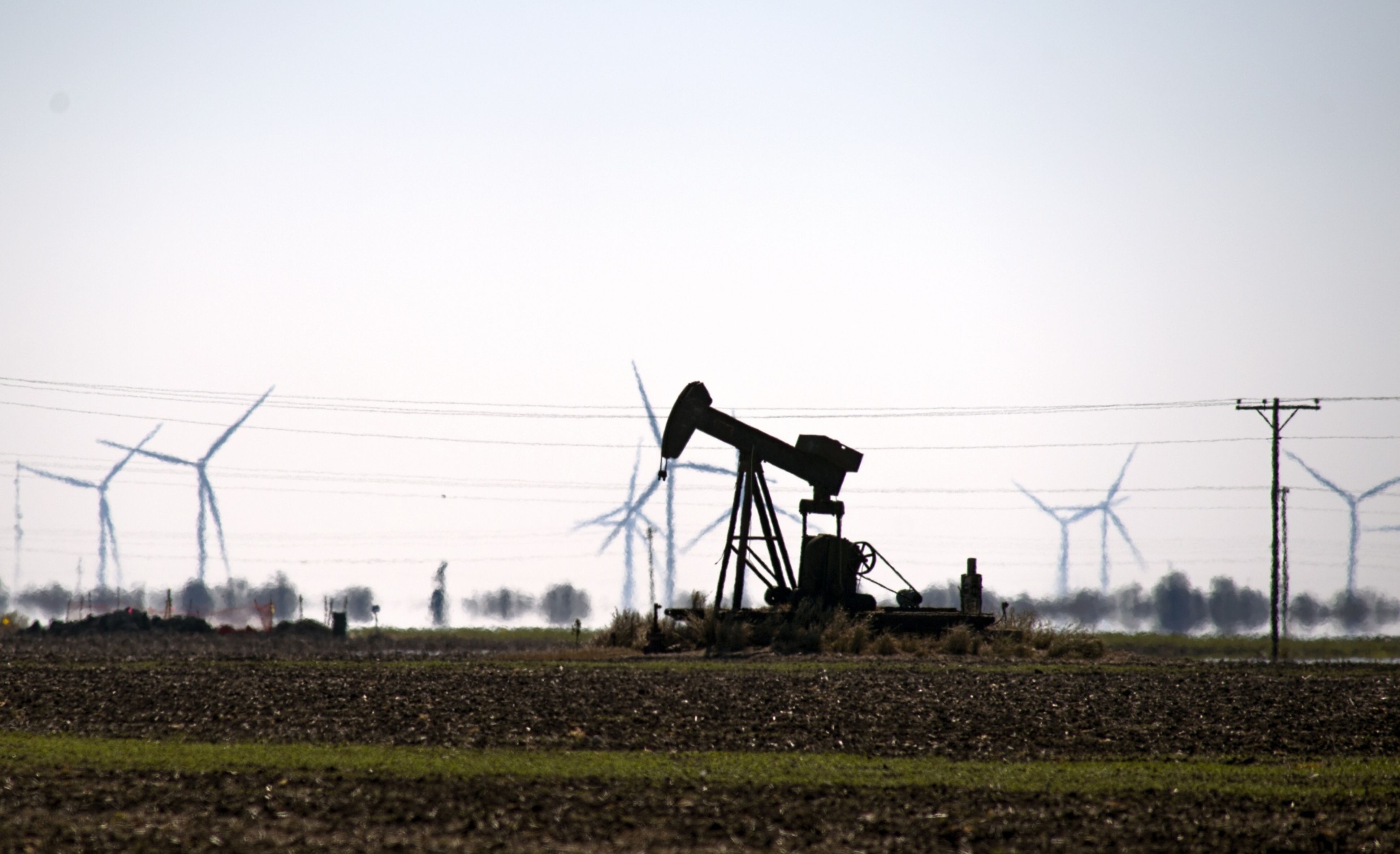 An oil pump jack in a field with wind turbines in Corpus Christi, Texas, U.S., Friday, Feb. 19, 2021.