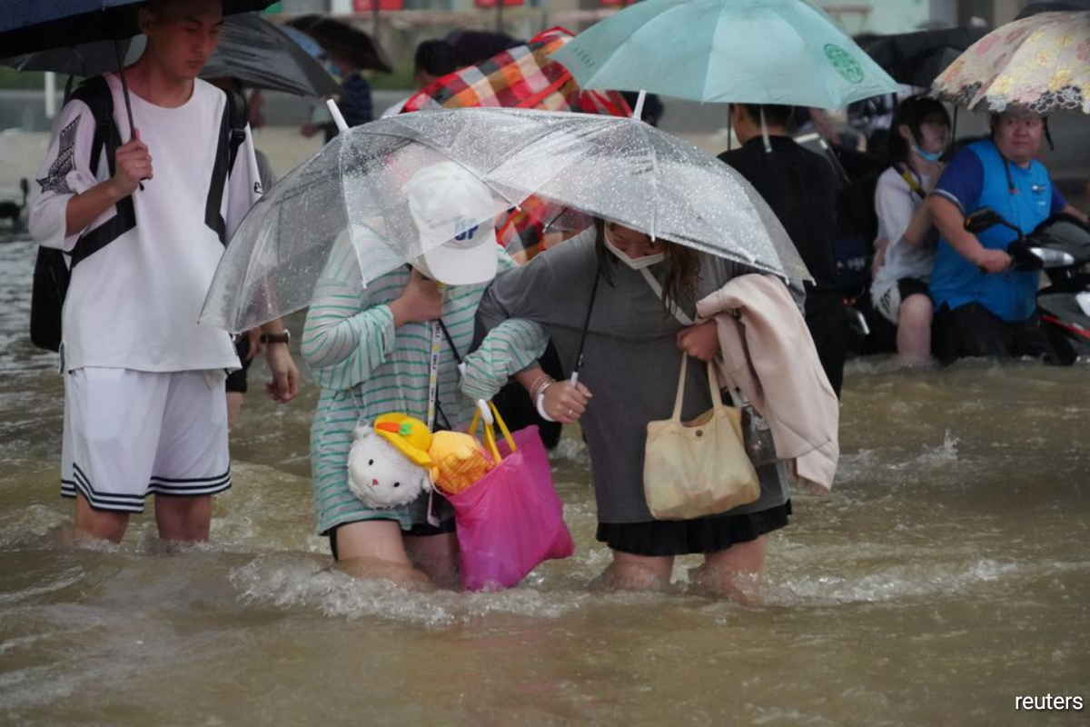 Residents, holding umbrellas amid heavy rainfall, wade through floodwaters on a road in Zhengzhou, Henan province, China.