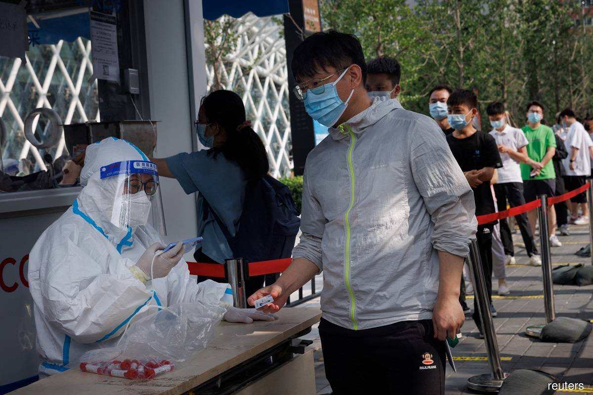 A worker in a protective suit scans the identification card of a man at a nucleic acid testing station, following a Covid-19 outbreak, in Beijing, China, June 29, 2022.